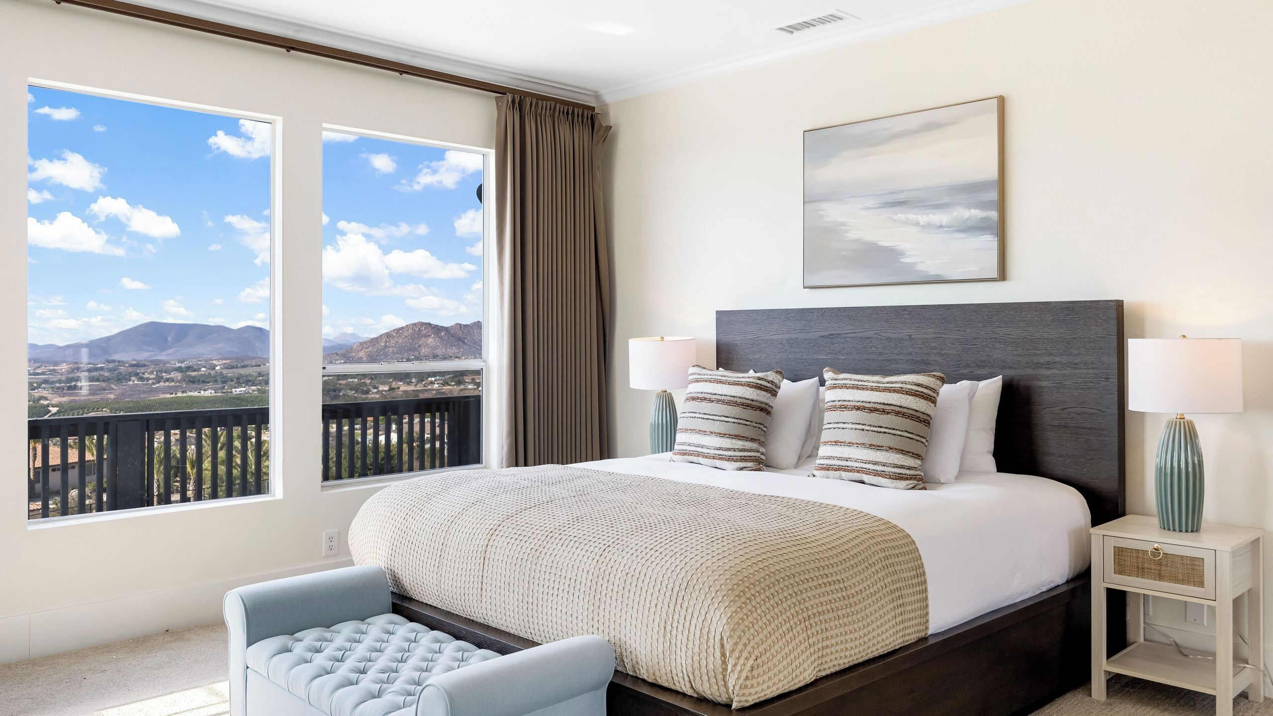 A bedroom with a large bed, two bedside lamps, a view of mountains, and a balcony.