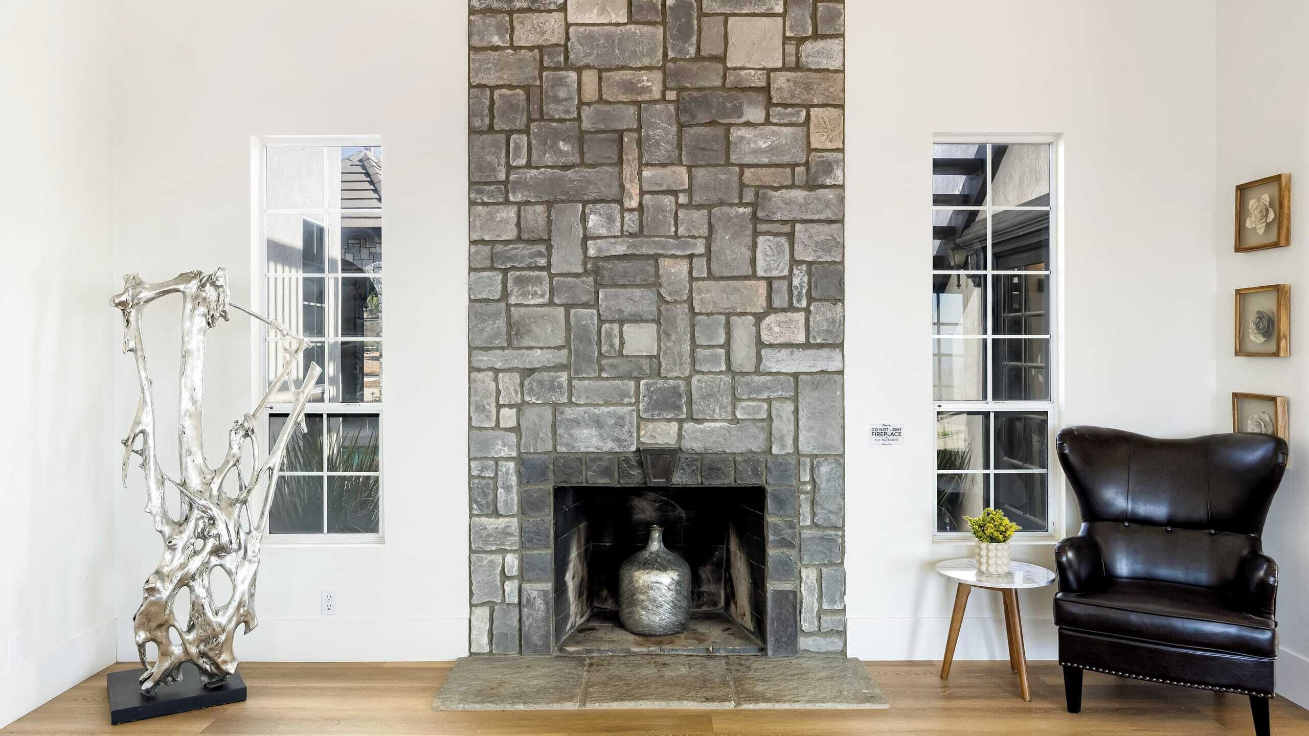 A living room with a stone fireplace, a black leather chair, and a sculpture on the left.
