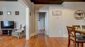 A spacious living room with hardwood flooring, a television, a green armchair, and a dining area with wooden chairs and a table. - Park Avenue Retreat (Hot Springs)