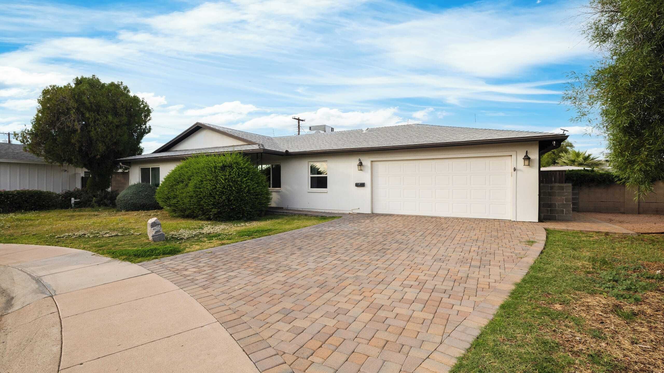 A single-story house with a garage, a brick driveway, and a well-maintained lawn.