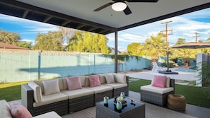 An outdoor patio with a sofa, wicker furniture, a pool, and a view of the backyard.
