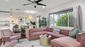 A modern living room with a pink sofa set, a dining area with a wooden table, and a kitchen with white cabinets. - Scottsdale Retreat w/ Private Pool, Outdoor Dining & Close to Old Town Fun Casa Cambridge by Avantstay (Scottsdale)