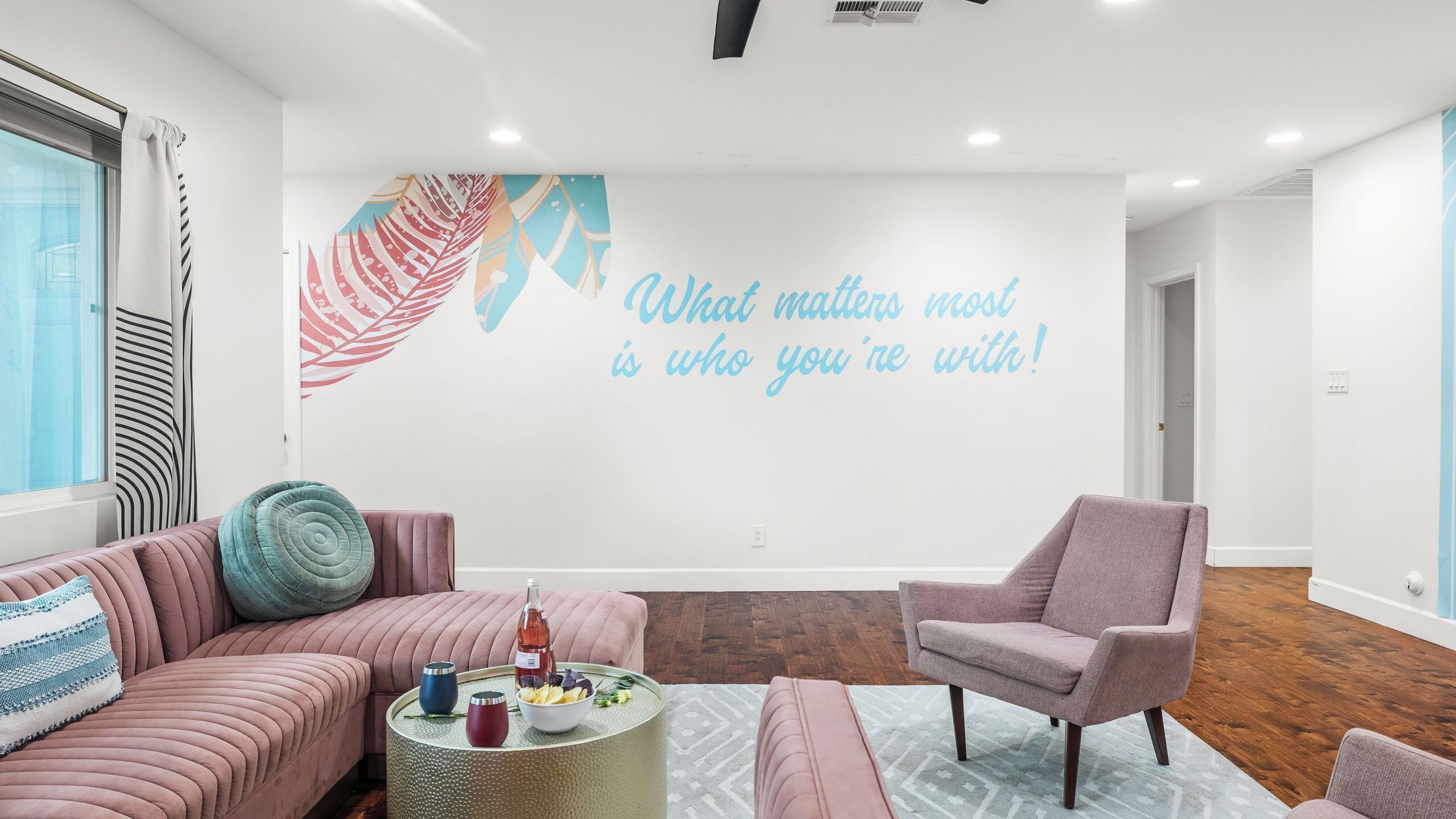 A modern living room with a large wall mural, a pink sofa, a round coffee table, and a pink armchair.