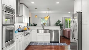 A modern kitchen with stainless steel appliances, white cabinetry, a central island, and a view of greenery outside.