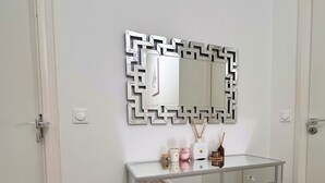 A bathroom with a white vanity, a geometric mirror, and a wooden floor. - Premium Room Paris La Défense Arena (Nanterre)