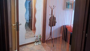 Una habitación con suelo de baldosas, una puerta de madera, un espejo, una pequeña estatua y una cortina.