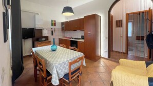 Cocina compacta con armarios de madera, una mesa de comedor con sillas y un televisor montado en la pared.