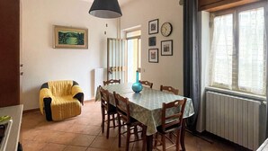 Un comedor con una mesa redonda, sillas, una lámpara colgante y un ventanal con cortinas.
