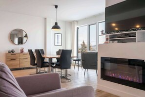Een moderne woonkamer met een open haard, eethoek en grote ramen.