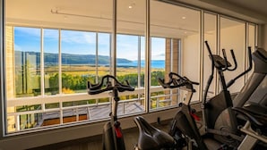 Un gimnasio con bicicletas estáticas y una cinta de correr, ventanas amplias con vistas al paisaje.