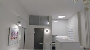 Une cuisine moderne avec des meubles blancs, un îlot central doté d’un banc et un lustre décoratif.
