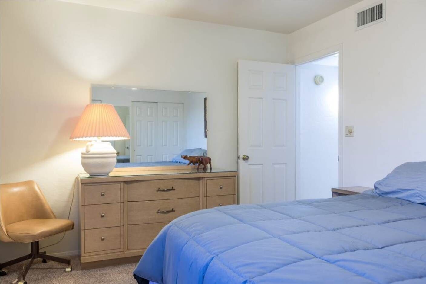A bedroom with a bed, a dresser, a chair, and a lamp.