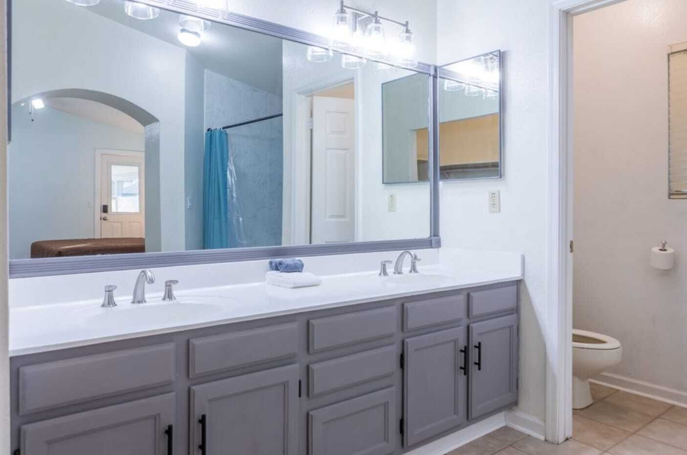 A bathroom with a large mirror, two sinks, and a toilet.