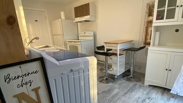 Una cucina compatta con elettrodomestici bianchi, un piccolo angolo ristoro e un cartello con la scritta 'Bienvenue chez NUS'.