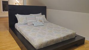 Una camera da letto moderna con una testiera scura, un letto con biancheria a motivi e un pavimento in legno.