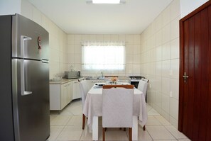A compact kitchen with a refrigerator, stove, microwave, and dining table set for four. - Casa com piscina a 250m da Praia PLH006 (Palhoça)