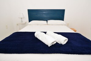 Una cama con cabecera azul, almohadas blancas y una manta azul oscuro.