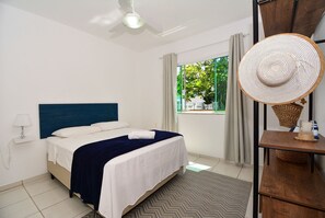 A bedroom with a bed, a ceiling fan, a window with curtains, and a view of greenery outside. - Casa com piscina a 250m da Praia PLH006 (Palhoça)