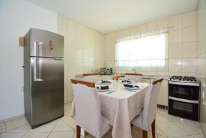 Una cocina con un refrigerador de acero inoxidable, una mesa de comedor dispuesta con platos, vasos y un florero con flores.