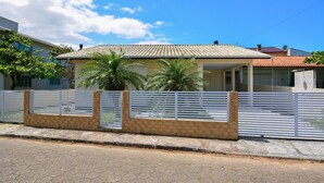 A residential house with a tiled roof, a fenced yard, and a paved driveway. - Casa com piscina a 250m da Praia PLH006 (Palhoça)