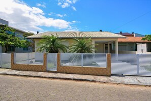 A residential house with a tiled roof, a fenced yard, and a paved driveway. - Casa com piscina a 250m da Praia PLH006 (Palhoça)