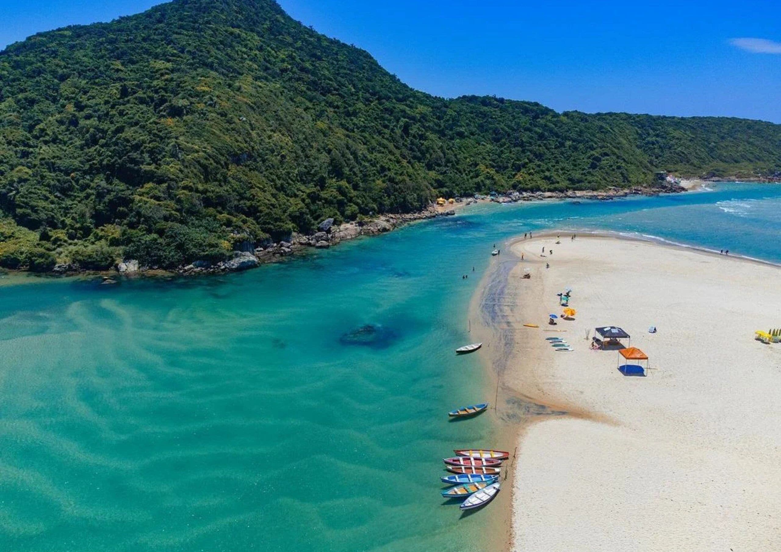 A beach with clear turquoise waters, a sandy shore, and a lush green mountain in the background.