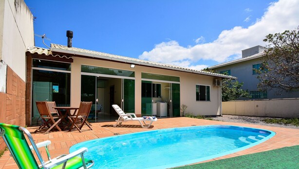 A swimming pool with a patio area, including a chair and a table. - Casa com piscina a 250m da Praia PLH006 (Palhoça)
