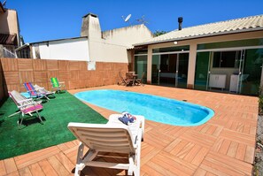 Un patio trasero con piscina, un área de patio con sillas y una mesa, y un porche cubierto con una mesa y sillas.