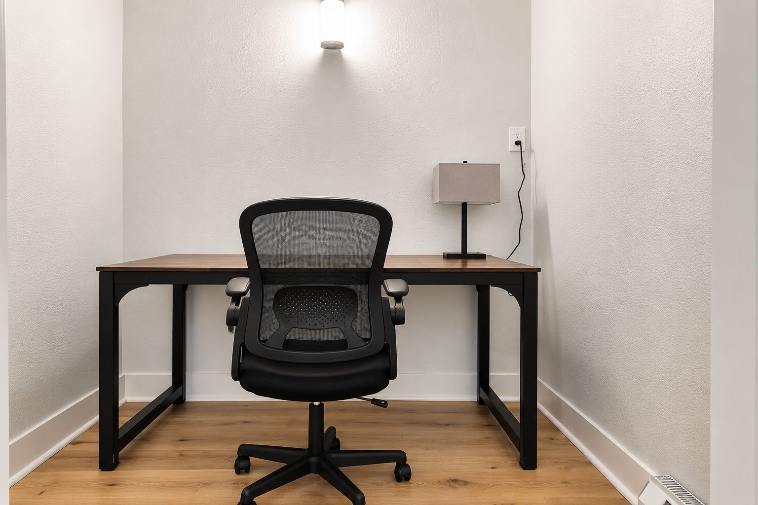 Ein Büro im Eck mit Schreibtisch, Stuhl und Wandlampe.