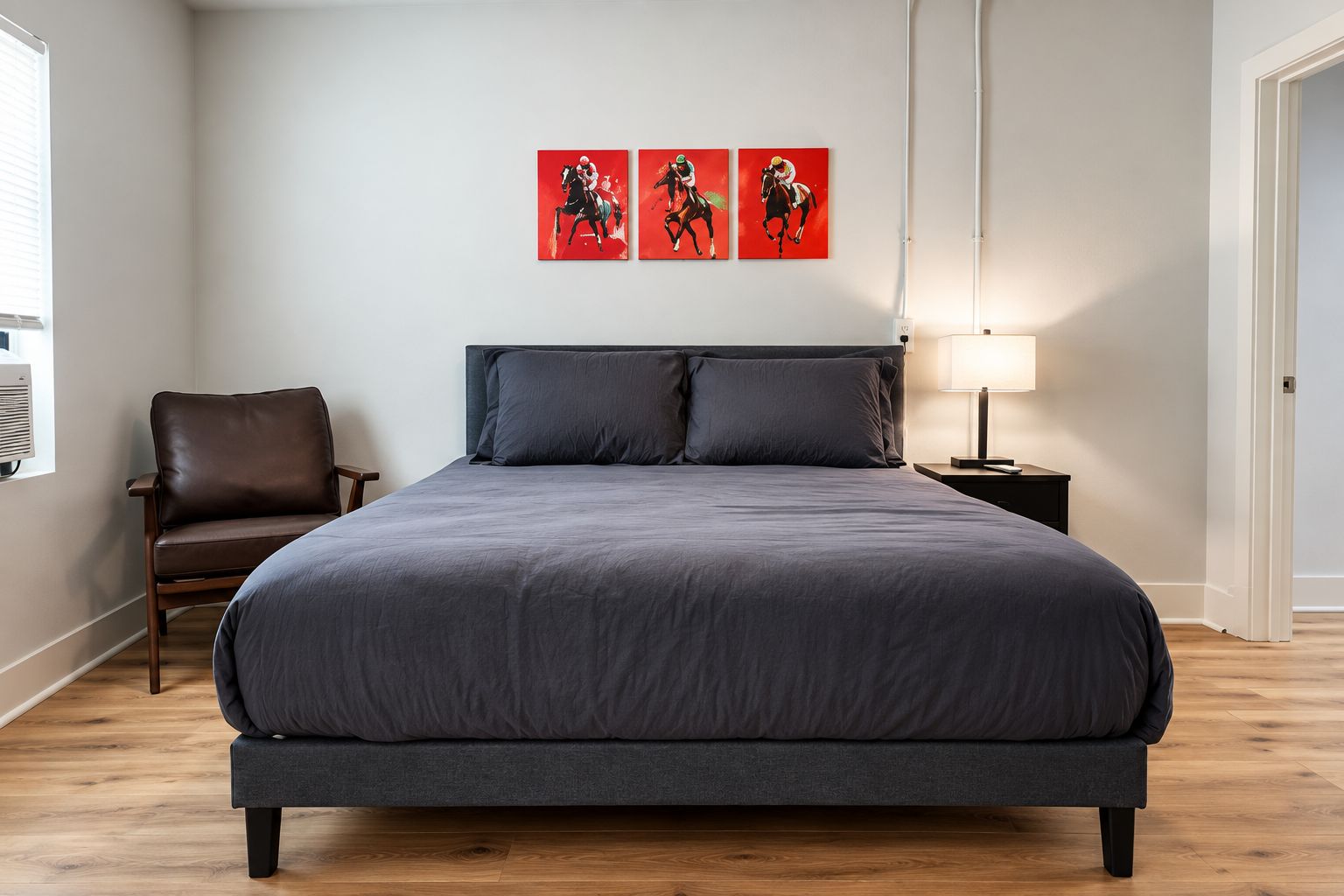 Ein Schlafzimmer mit einem großen Bett, einem Sessel, einem Nachttisch und drei roten Kunstwerken an der Wand.