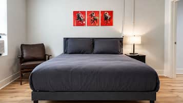 Ein Schlafzimmer mit einem großen Bett, einem Sessel, einem Nachttisch und drei roten Kunstwerken an der Wand.