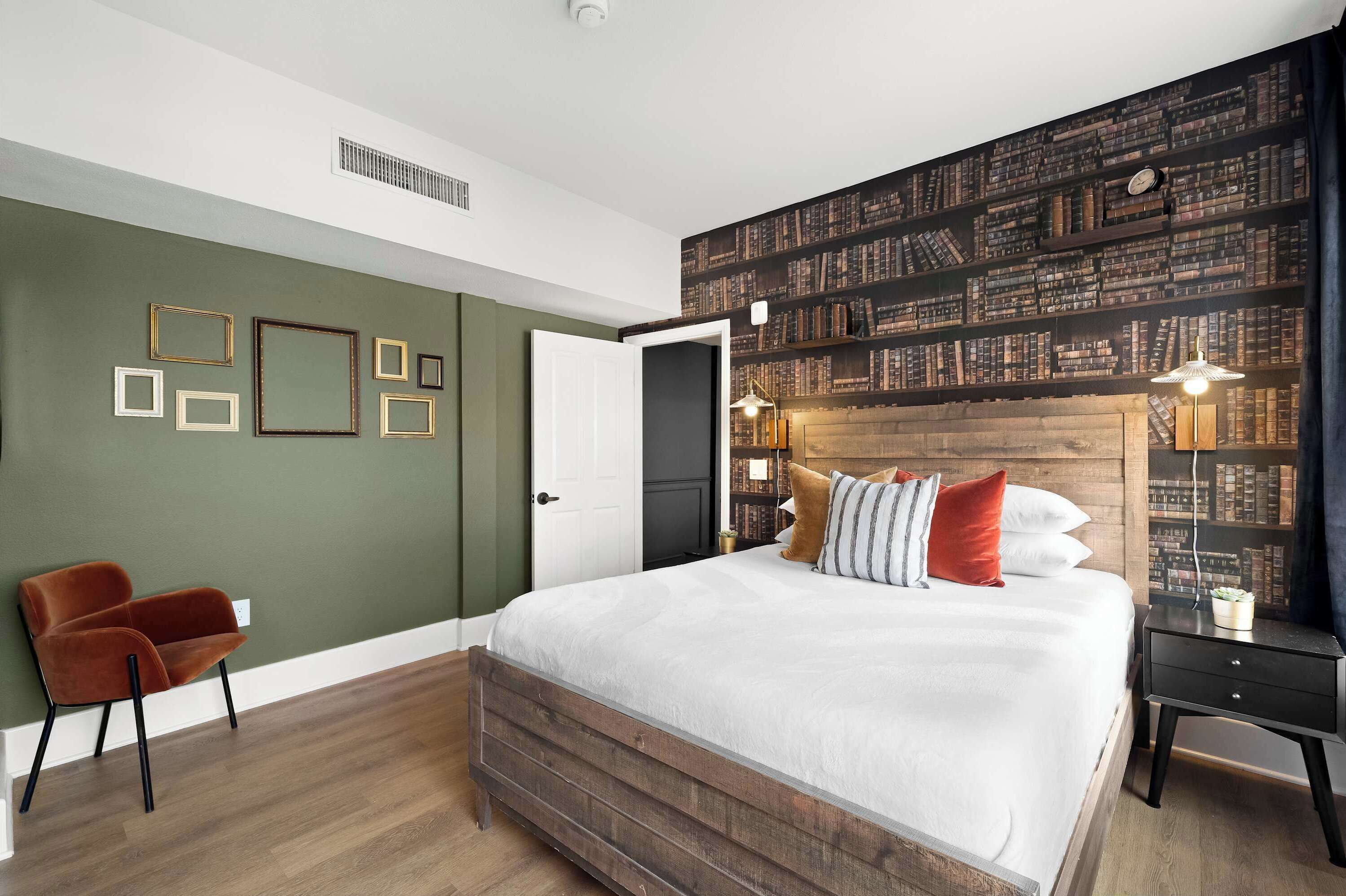 A bedroom with a large bed, a chair, a nightstand, a bookshelf, and a door.