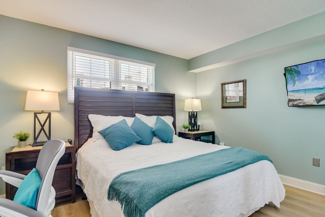 Une chambre à coucher comprenant un lit, des tables de chevet, une chaise, une fenêtre avec des stores et un tableau accroché au mur.