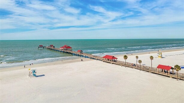 Una playa con un muelle de madera que se adentra en el océano, con edificaciones de techo rojo a lo largo de su extensión.