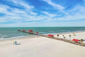 Una playa con un muelle de madera que se adentra en el océano, con edificaciones de techo rojo a lo largo de su extensión.