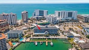 Un hotel frente al mar con varias construcciones, un puerto deportivo con barcos y una vista despejada del océano.