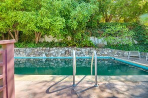 A swimming pool with metal ladders, surrounded by a stone wall and lush greenery. - Quiet LA Retreat with Pool and Patio (Los Angeles)