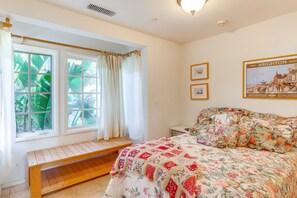 A bedroom with a wooden bench, a floral bedspread, and a window with curtains. - Quiet LA Retreat with Pool and Patio (Los Angeles)