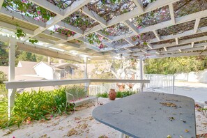 A covered patio area with a curved table, white railings, and hanging plants. - Quiet LA Retreat with Pool and Patio (Los Angeles)