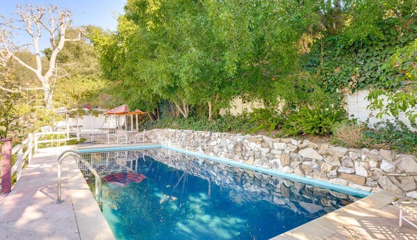 A swimming pool with a stone wall, surrounded by greenery and a gazebo. - Quiet LA Retreat with Pool and Patio (Los Angeles)