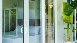 Una habitación moderna con una cama, puertas de vidrio correderas, una planta grande en maceta y un tapete tejido en el suelo.