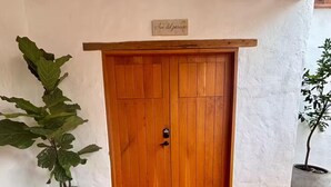 Eine Holztür mit einer Schilder über ihr und einem Blumentopf links, außerdem ein Fliesenboden.