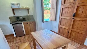 Eine kompakte Küche mit Holztisch und Bank, einem kleinen Kühlschrank und einem Fenster mit Blick auf einen Garten.