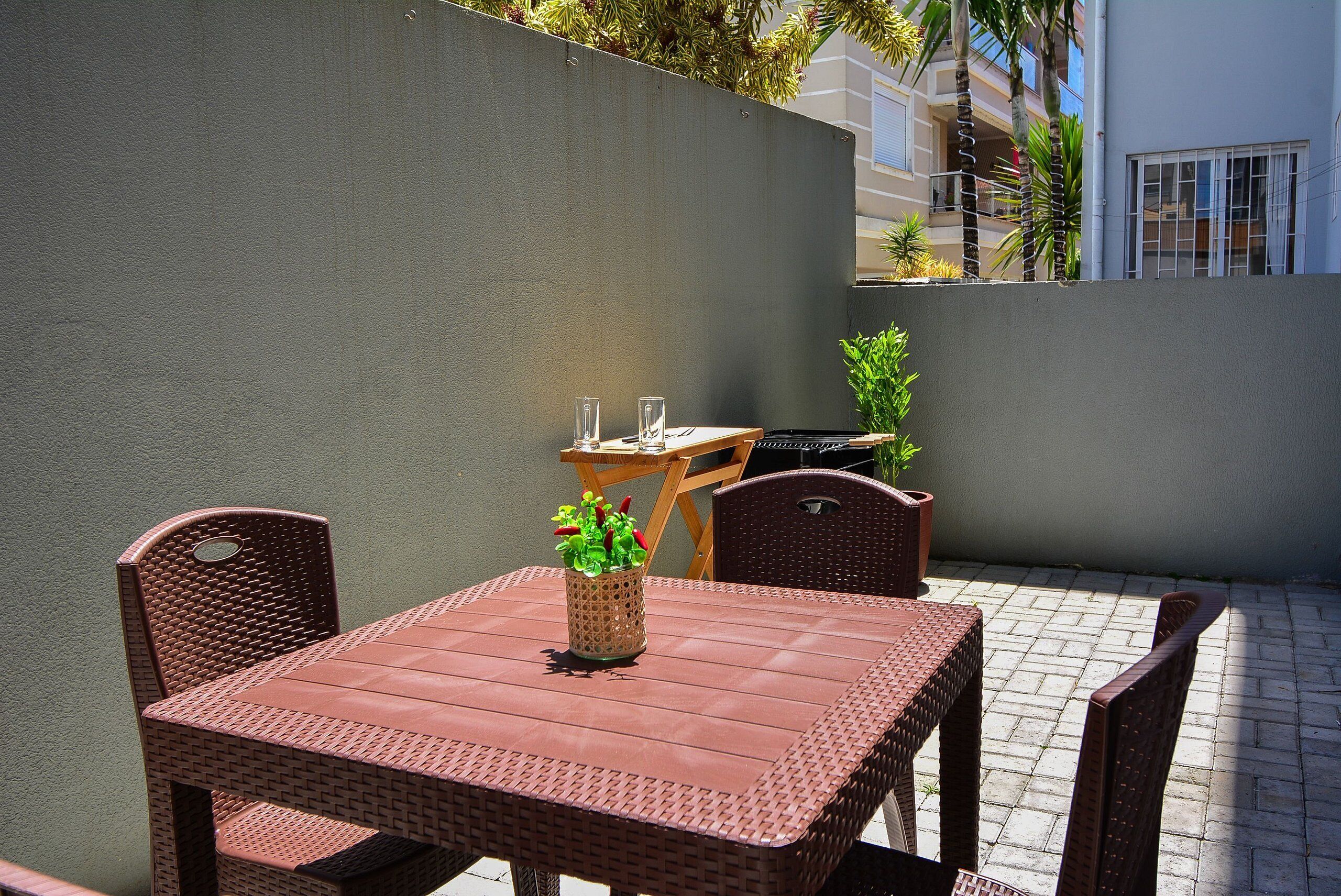 Un patio al aire libre con una mesa y sillas, una planta en maceta y una vista de un edificio al fondo.