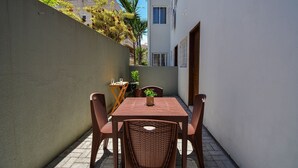Une terrasse avec une table et des chaises, une plante en pot et une petite table avec un verre.