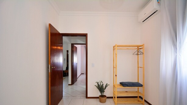 Un couloir avec une porte en bois, une plante en pot et un banc en bois agrémenté d’un coussin bleu.