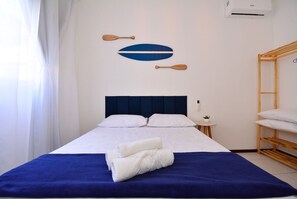 A neatly made bed with white linens and a blue accent, a small bedside table with a plant, and a wooden bunk bed to the right. - Refúgio do Mar Centrinho Ingleses-NIN017 (Florianópolis)