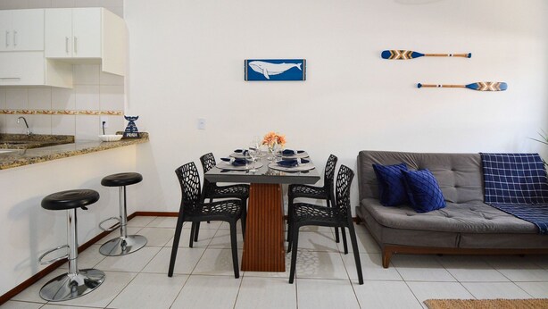 A modern kitchen with white cabinets, a dining table set for four, and two bar stools. - Refúgio do Mar Centrinho Ingleses-NIN017 (Florianópolis)