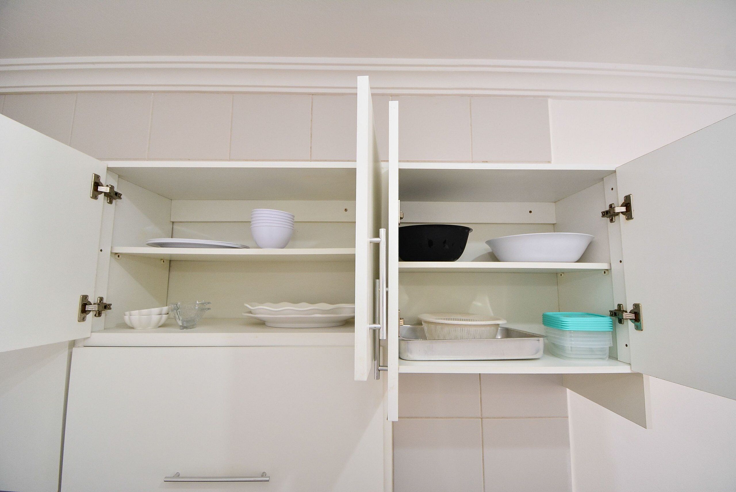 A white kitchen cabinet with open doors, revealing shelves with dishes and bowls.