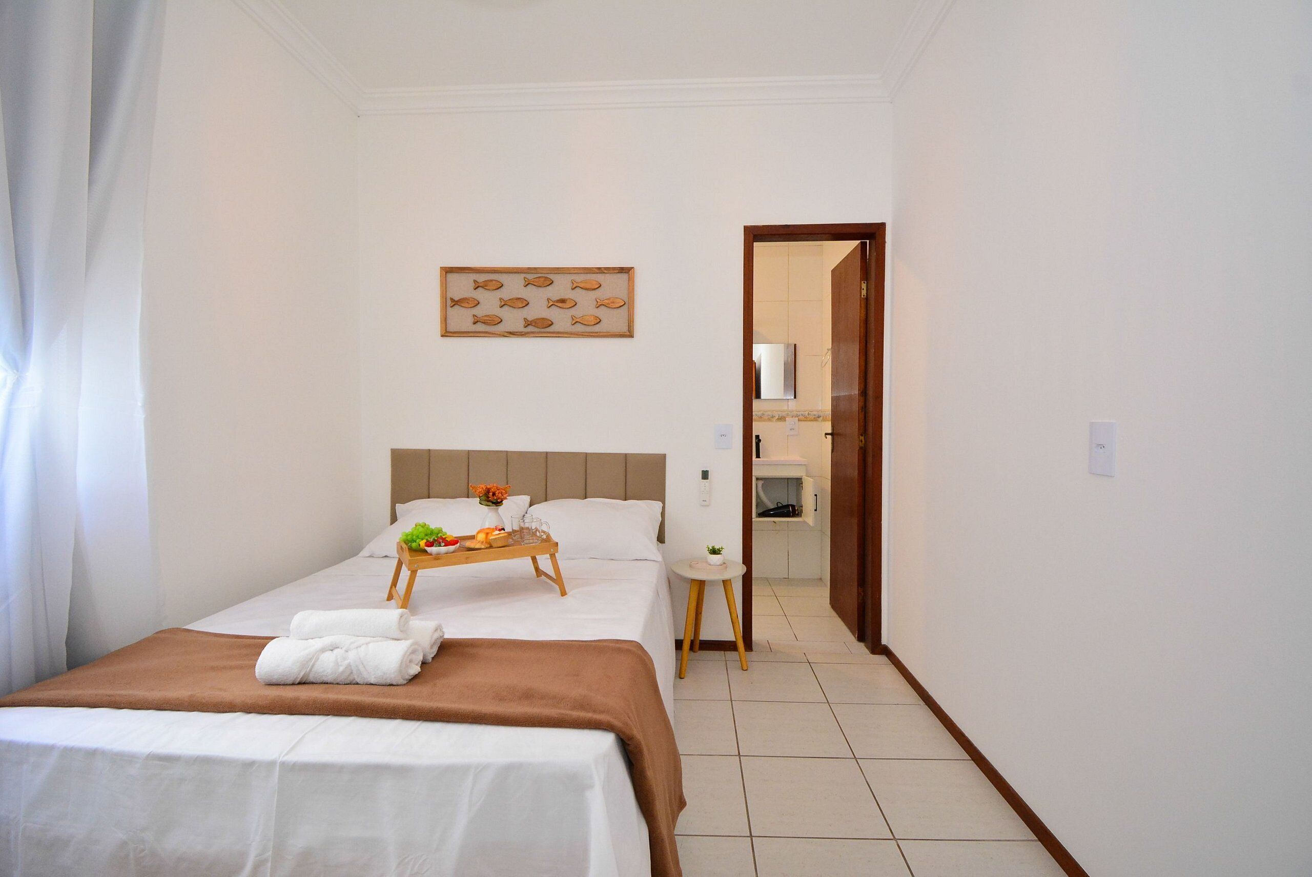 Habitación de hotel con cama, mesita de noche con bandeja, taburete pequeño y espejo en el baño.